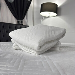 Protector de colchón en algodón 100%, color blanco, colocado sobre un colchón. Se muestra suave, ligero y ajustado a las esquinas, diseñado para proteger de manchas y ofrecer un descanso fresco